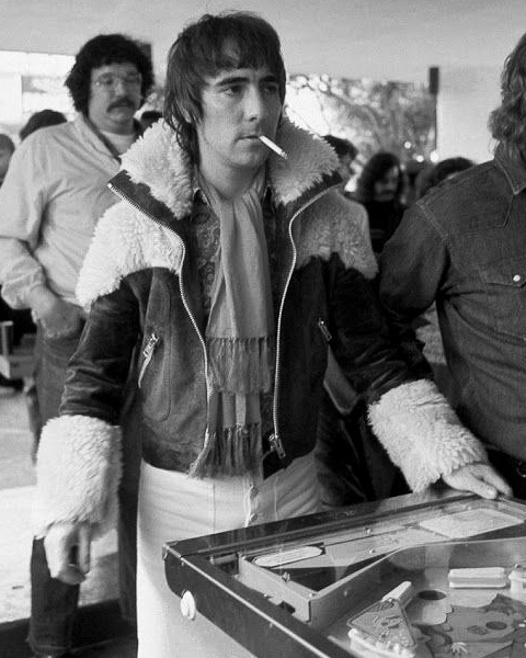 Rockstar playing on pinball machine with 80s style jacket