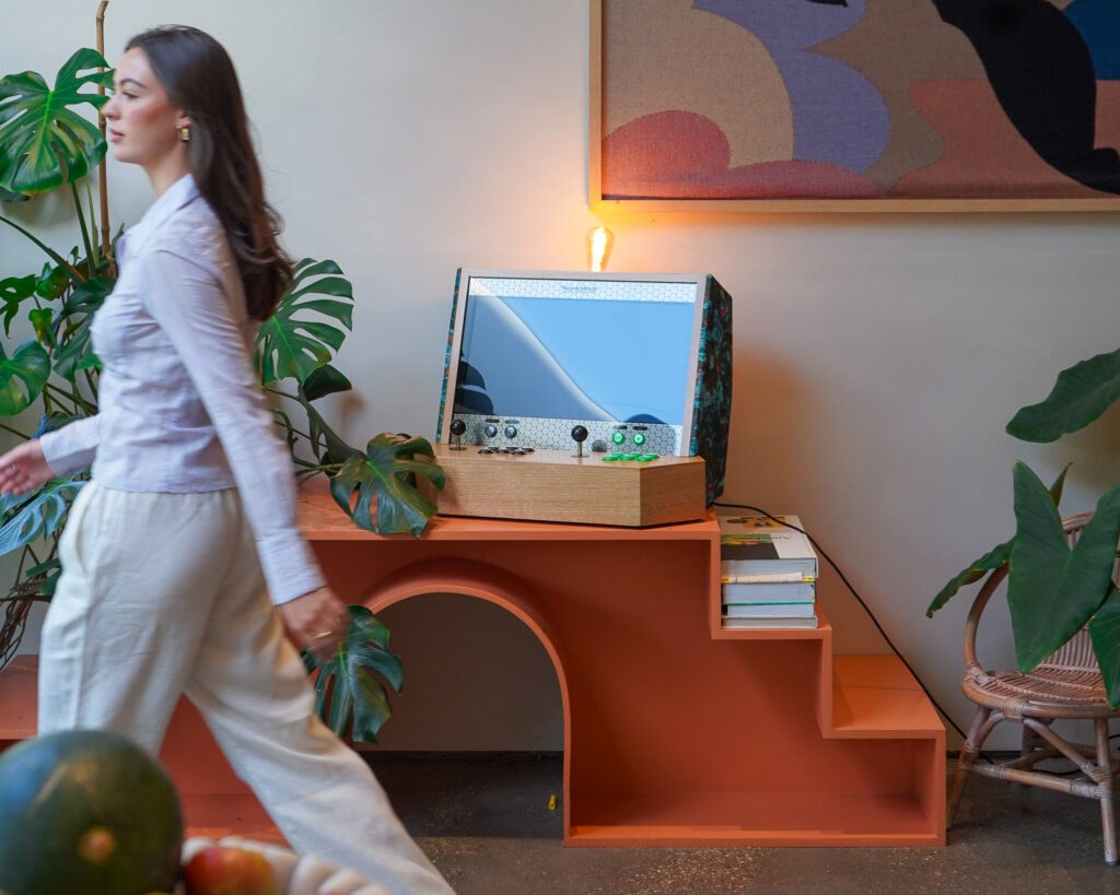 Orange side cabinet in unique shape with books, arcade and plants on it